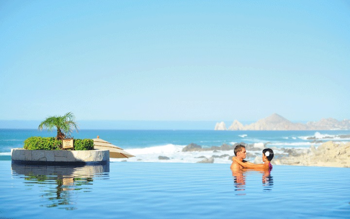 A honeymoon couple enjoying a romantic moment in an infinity pool overlooking the ocean at Hacienda Encantada Resort in Los Cabos, Mexico